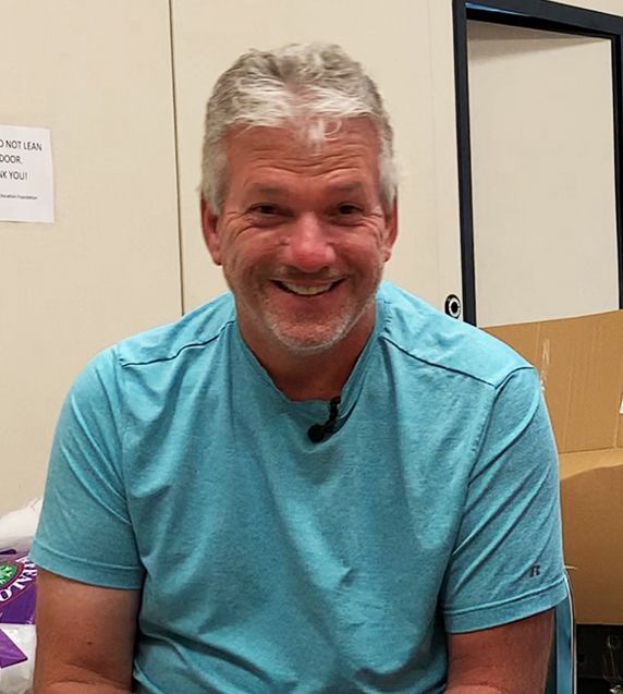 John Rose, voluntario de la Fundación de Educación de Hillsborough, hombre mayor en el aula sonriendo, vistiendo una camisa azul